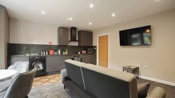 A compact living space with a kitchenette, a sofa, a dining area, and a flat-screen TV mounted on the wall.