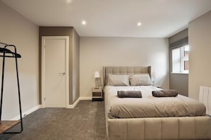 A bedroom with a bed, bedside tables, a hanging light, and a window. - The Olive Tree Aparthotel | Deluxe Single Stay (Kingston upon Hull)
