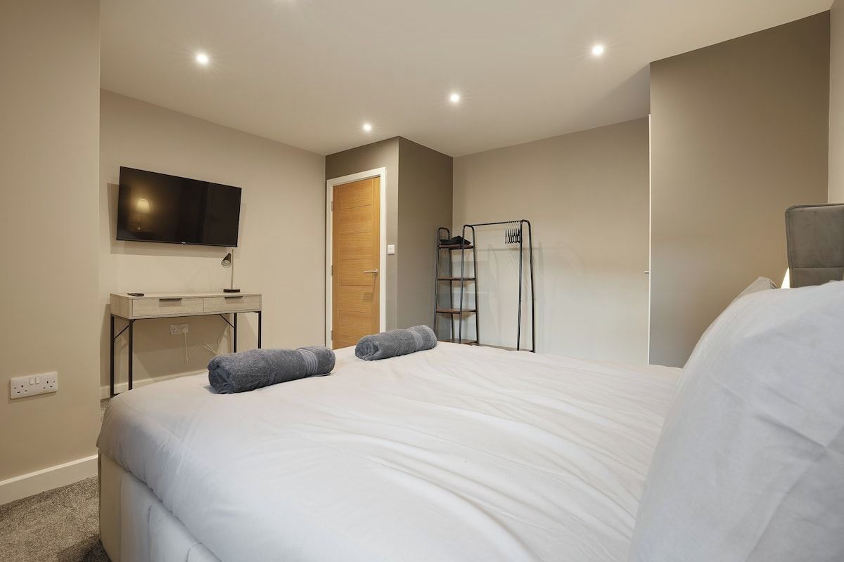 A hotel room with a bed, a TV mounted on the wall, a desk, and a wardrobe.