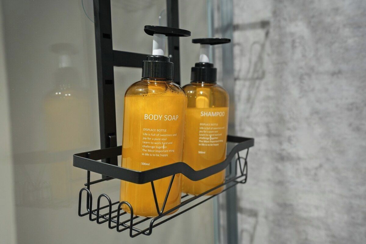 Two bottles of body soap and shampoo on a black shelf.