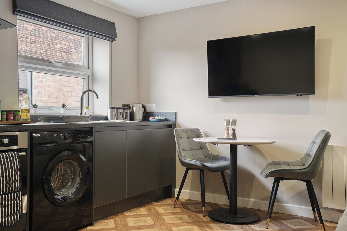 A compact kitchen with a washing machine, a sink, a stove, and a flat-screen TV mounted on the wall.