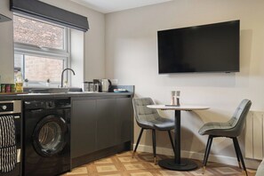 A compact kitchen with a washing machine, a sink, a stove, and a flat-screen TV mounted on the wall. - The Olive Tree | Deluxe 2-Bed Apartment (Kingston upon Hull)