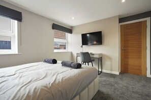 A bedroom with a bed, a desk, a chair, a television, and a door. - The Olive Tree | Deluxe 2-Bed Apartment (Kingston upon Hull)