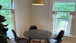 Ein Essbereich mit einem runden Tisch, vier Stühlen, einer Hängeleuchte und großen Fenstern mit Vorhängen.