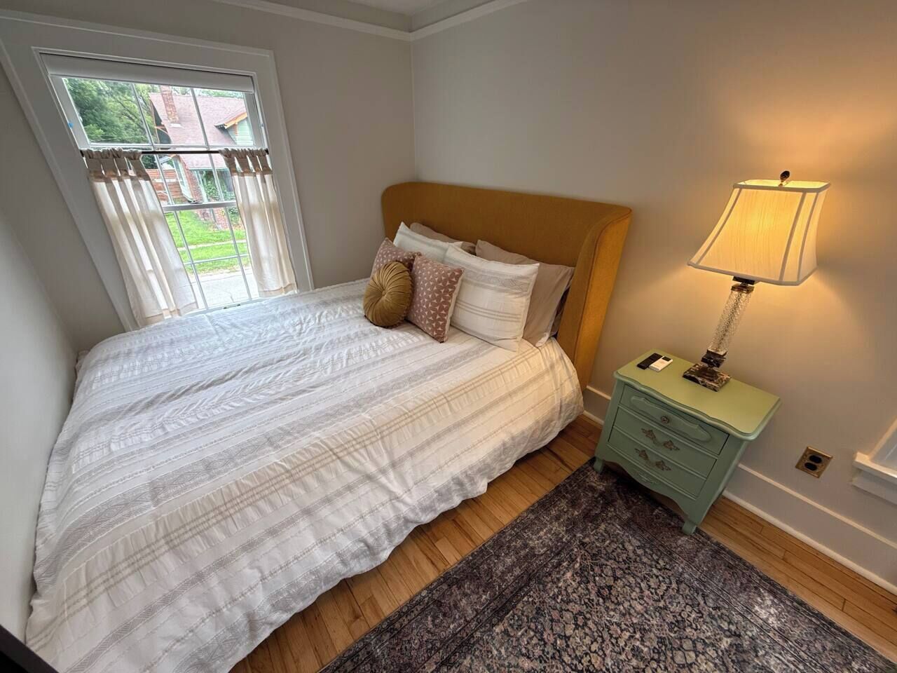 A bedroom with a bed, a nightstand, a lamp, and a window with curtains.