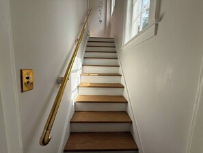 A staircase with wooden steps and a brass handrail, leading to a landing with a door and a light switch.