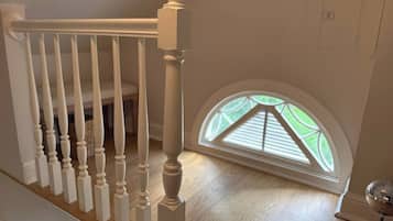 A staircase with white balusters leading to a landing, a small round table with a decorative item, and a skylight with a view of greenery.
