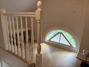 A staircase with white balusters leading to a landing, a small round table with a decorative item, and a skylight with a view of greenery. - The Hayloft - Newly Renovated Historic Home + EV (Fairfield)