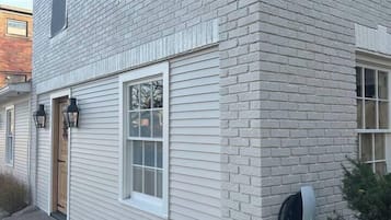 A two-story building with a white brick facade, a wooden door, and a black outdoor light fixture.
