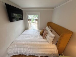 A bedroom with a bed, a window with curtains, and a mounted television. - The Hayloft - Newly Renovated Historic Home + EV (Fairfield)