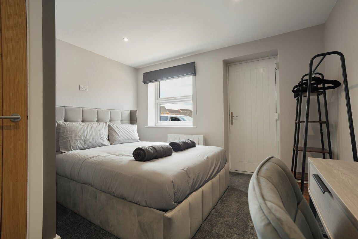 A bedroom with a bed, a window, a door, and a desk.