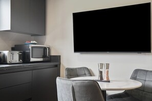 A modern kitchen with a flat-screen TV, a microwave, and a toaster. There is a round table with two chairs and two salt shakers on the table. - The Olive Tree | Cozy Deluxe 2-Bed (Kingston upon Hull)