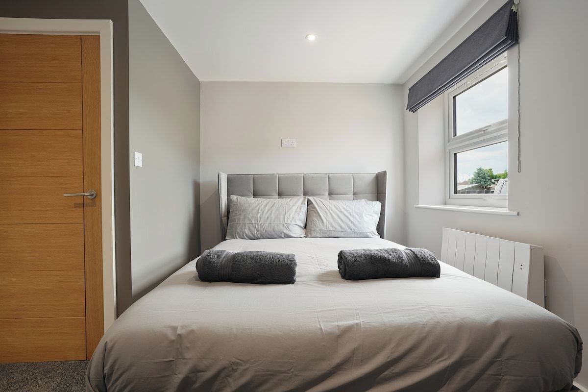 Een slaapkamer met een bed, een houten deur, een raam met zonwering en een radiator.