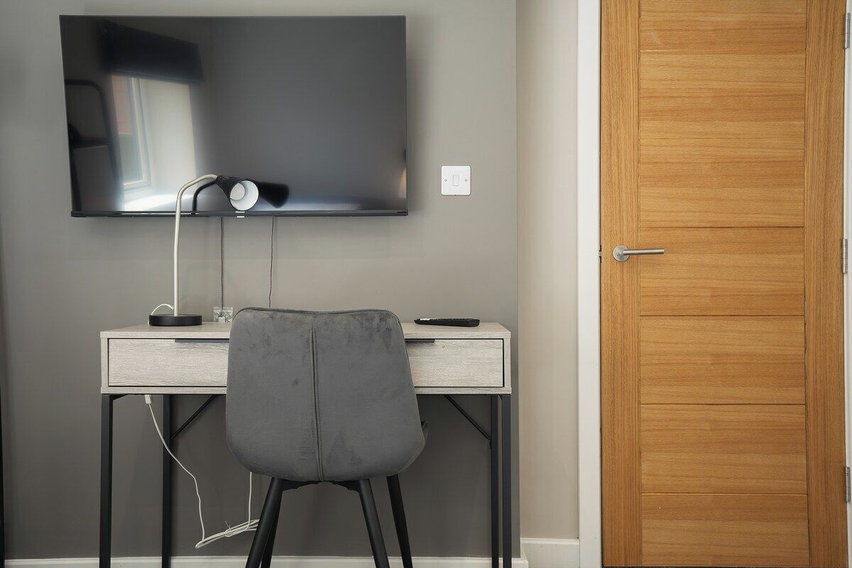 Une pièce dotée d’un téléviseur à écran plat fixé au mur, d’un bureau avec une chaise et d’une porte en bois.