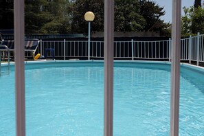 A clear swimming pool with a white fence, a yellow ball, and lounge chairs.