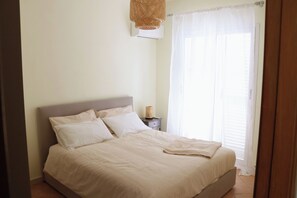 Un dormitorio con cama, mesita de noche y ventana con cortinas.