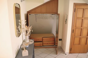 Een slaapkamer met een houten garderobe, een spiegel, een vaas met gedroogde bloemen en een klein tafeltje met lades.