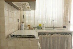 A kitchen with a gas stove, a sink, and a window with sheer curtains.