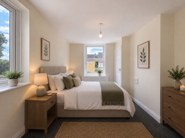 A bedroom with a bed, bedside table, lamp, and a view of the outside through a window.