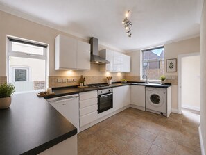 A modern kitchen with white cabinetry, a gas stove, a built-in oven, a dishwasher, and a window providing natural light.