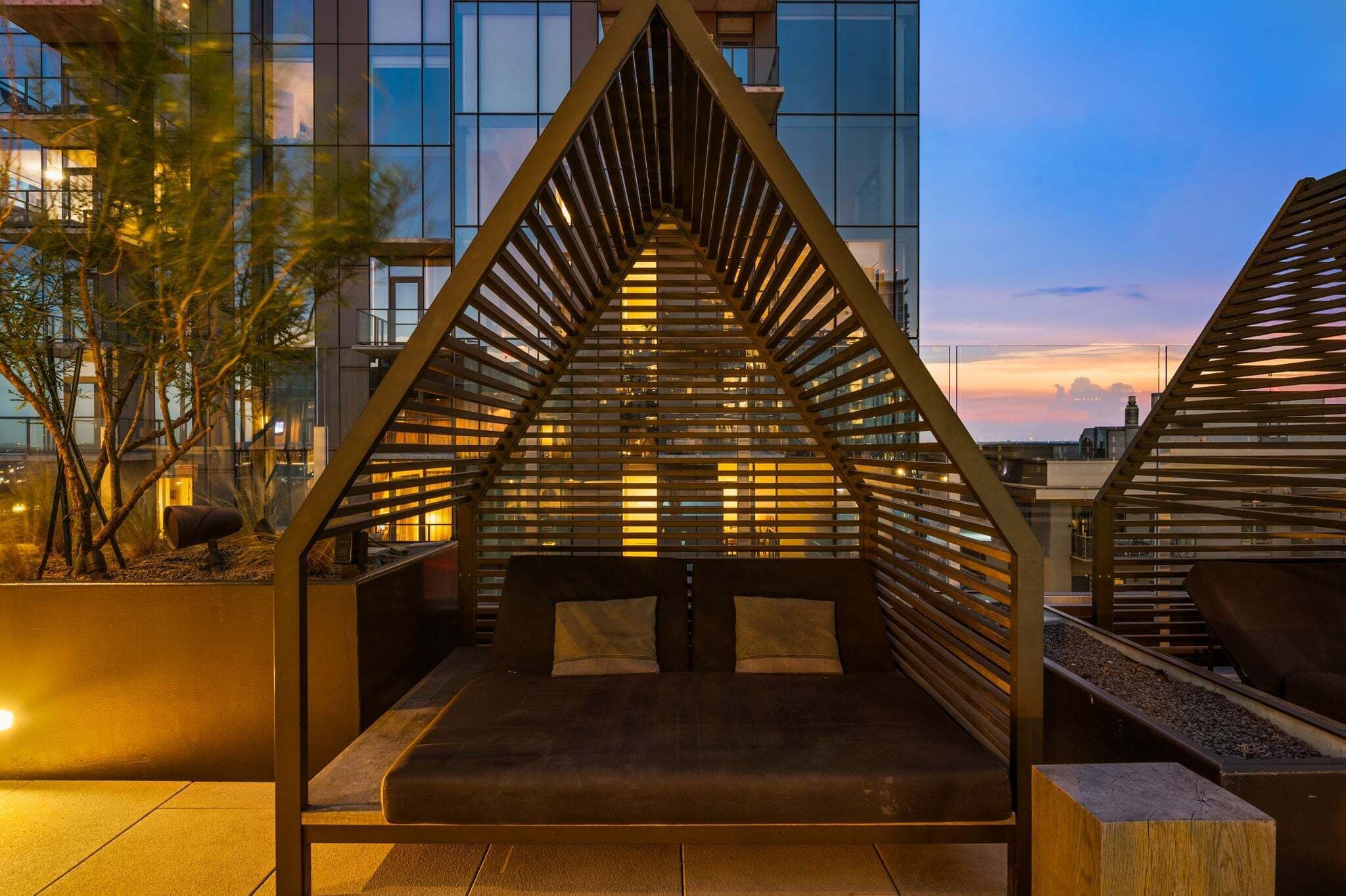 A modern outdoor seating area with a geometric metal structure, surrounded by a building with large windows.