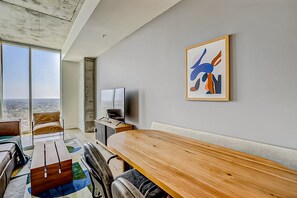 A modern hotel room with a large window, a wooden dining table, a sofa, and a television. - 24th-floor 1BR Sleeps 4 | Rainey + Rooftop Pool (Austin)