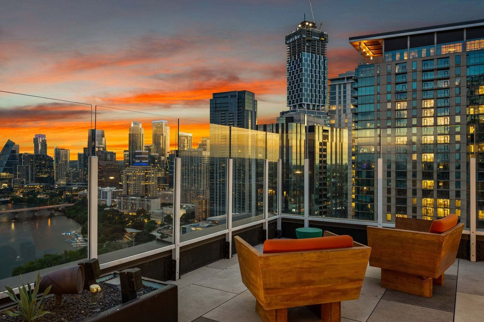 A rooftop terrace with a city skyline view, modern furniture, and a glass railing.