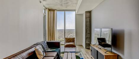 Una sala de estar moderna con un sofá, una mesa de centro, un televisor y vistas de la ciudad.