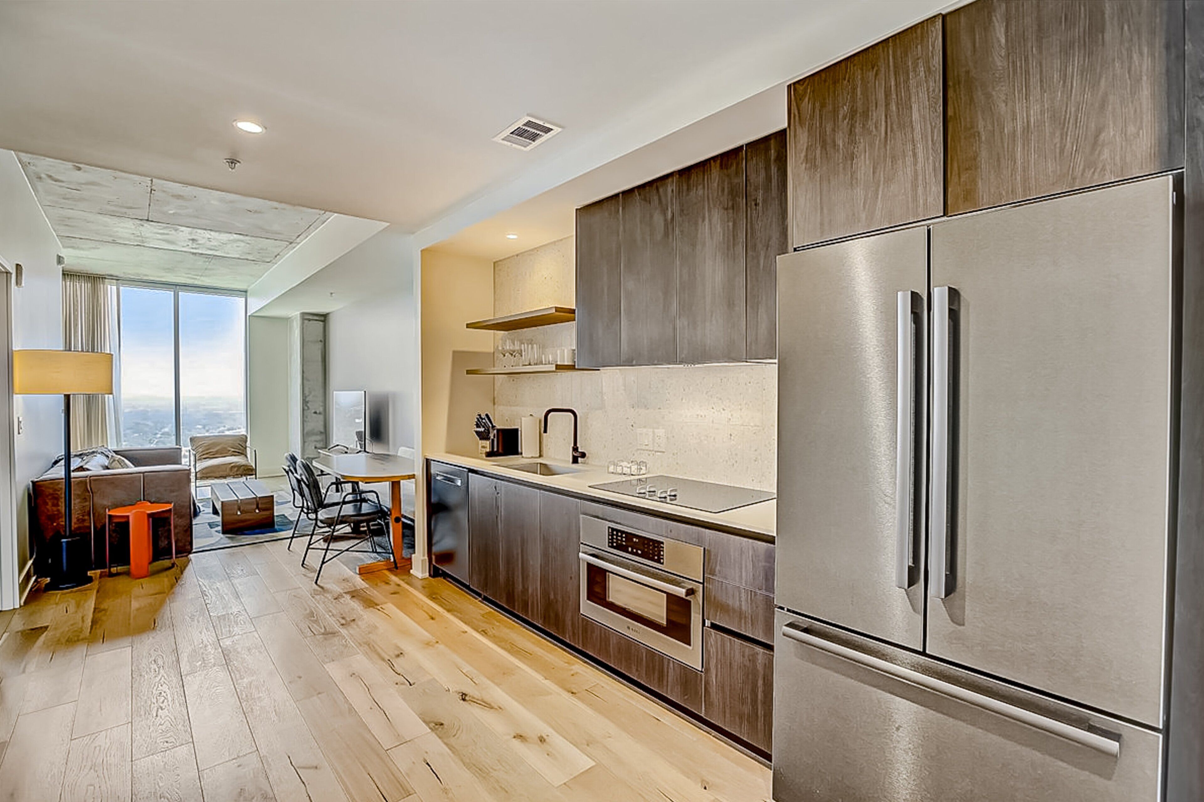 A modern kitchen with a large stainless steel refrigerator, a built-in oven, and a dining area with a table and chairs.