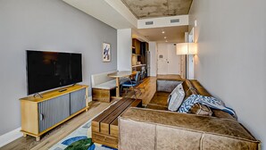 A modern living room with a flat-screen TV, a sofa, a dining area, and a kitchen in the background. - 24th-floor 1BR Sleeps 4 | Rainey + Rooftop Pool (Austin)