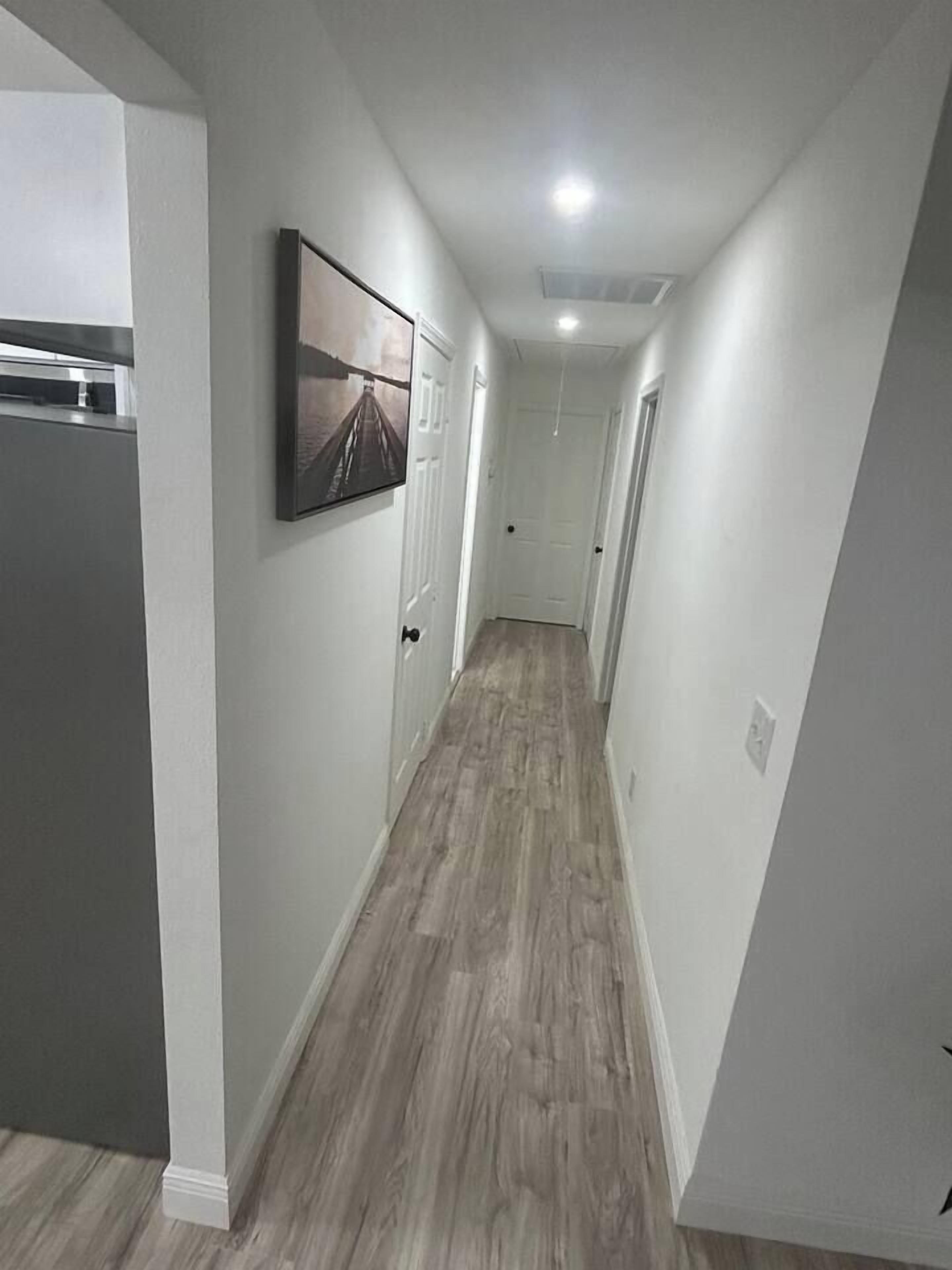 A narrow hallway with a wooden floor, white walls, and a framed picture on the wall.