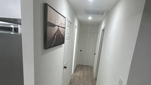 Un couloir étroit doté d’un plancher en bois, de murs blancs et d’un tableau encadré accroché au mur.