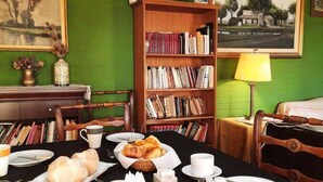A dining area with a table set for breakfast, a bookshelf, and a painting on the wall.