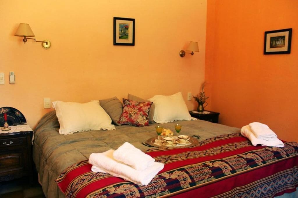 Habitación de hotel con cama, almohadas, mesita de noche, lámpara y un cuadro colgado en la pared.