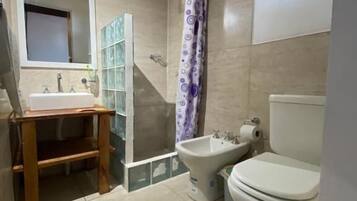 Un baño con inodoro, bidé, lavabo y un pequeño estante de madera.