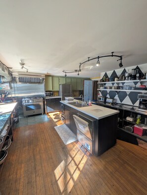 A modern kitchen with stainless steel appliances, wooden flooring, and a central island.