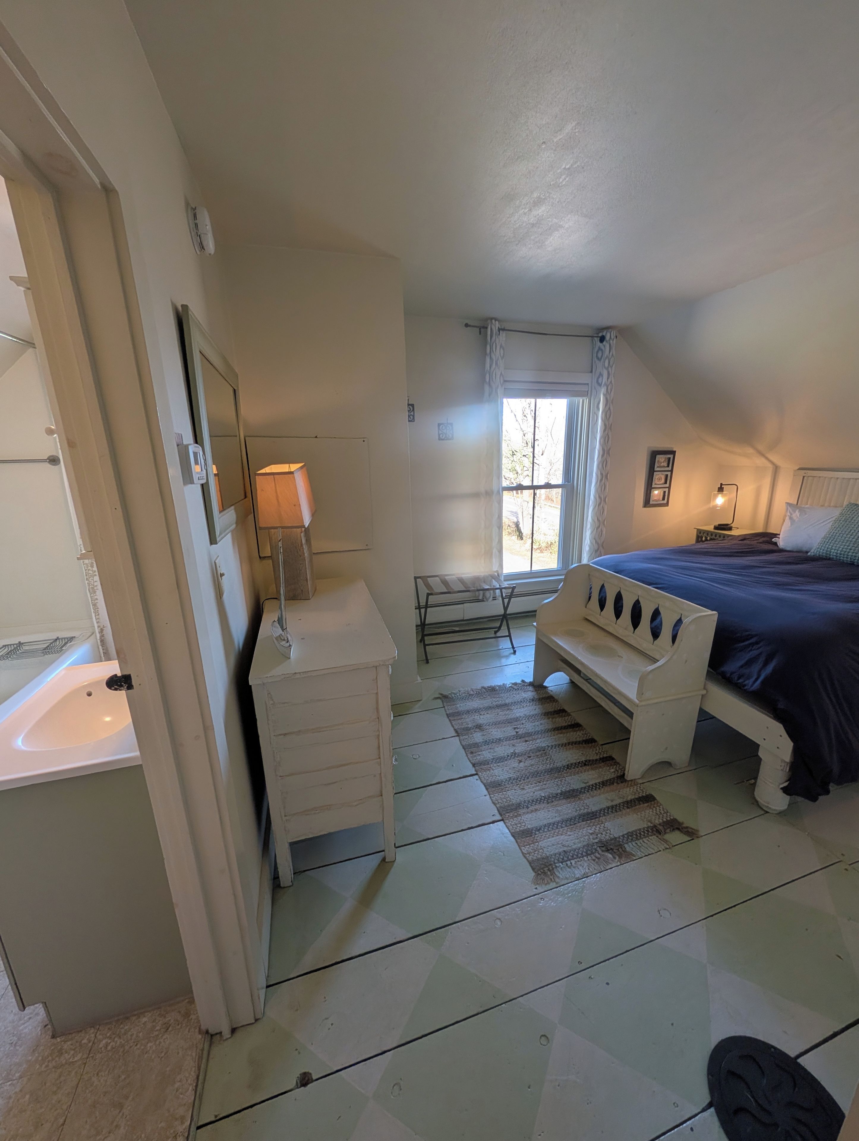 Un dormitorio con cama, mesita de noche, lámpara, ventana con cortinas y radiador.
