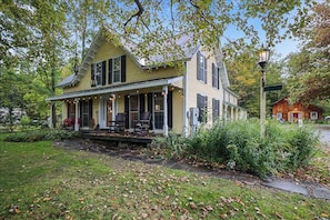 A two-story house with a porch, surrounded by greenery and a small shed.