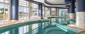 Ein Innenpool mit klaren Glaswänden, großen Fenstern und einem gefliesten Boden.