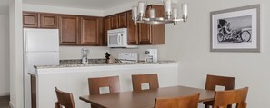 A kitchen with wooden cabinets, a white refrigerator, a microwave, a coffee maker, and a dining table with chairs. - Two-Bedroom Condo on Daytona Beach (Daytona Beach)