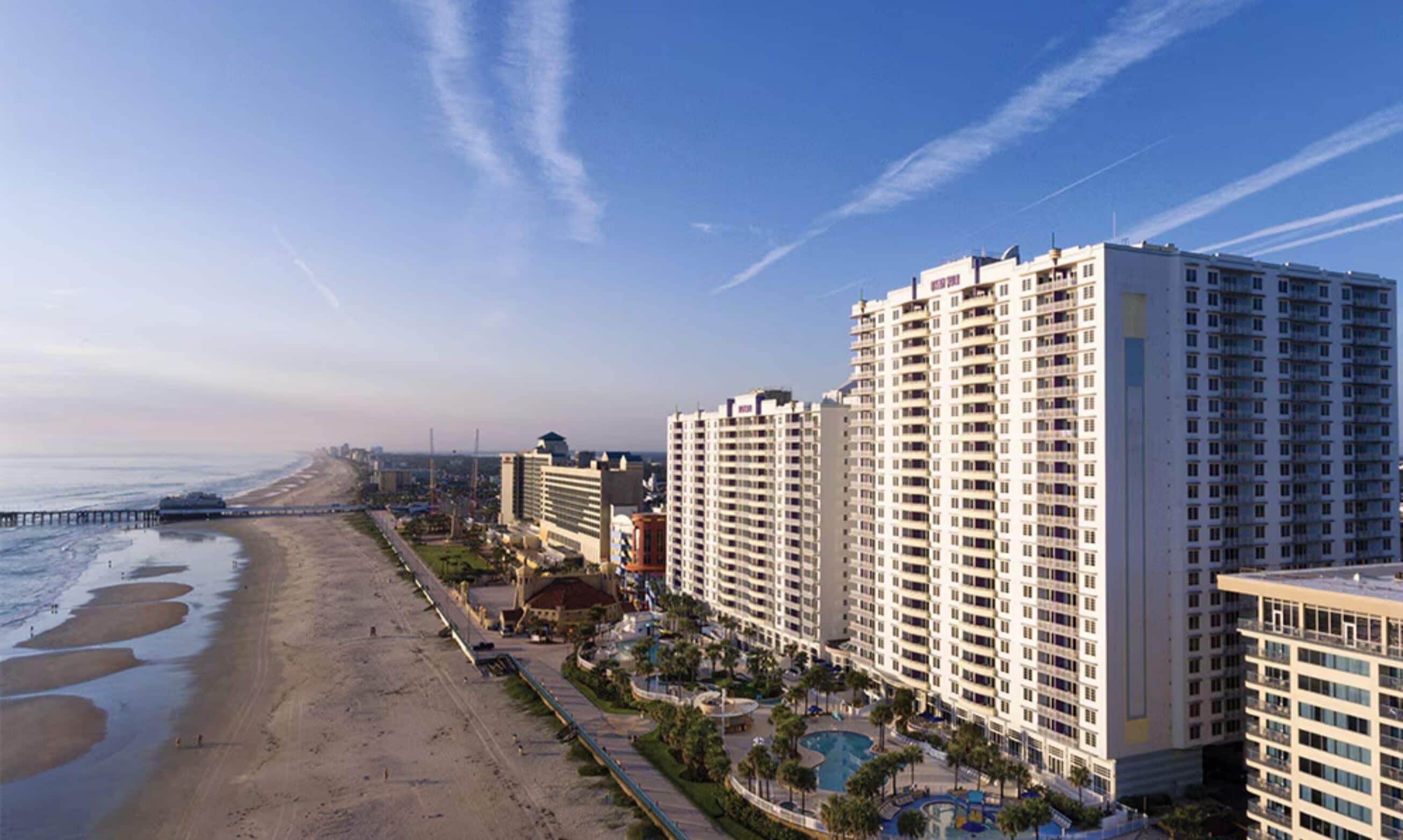 A beachfront hotel with multiple high-rise buildings, a sandy beach, and a pier extending into the ocean.