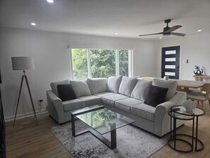 Un salon moderne avec un canapé d’angle, une table basse en verre et un ventilateur de plafond.