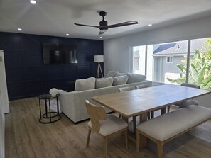 Ein modernes Wohnzimmer mit dunkler Akzentwand, einer Couch, einem Esstisch mit Stühlen und einem Deckenventilator.