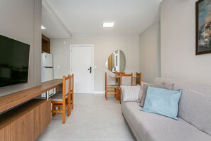 Un salon moderne avec un téléviseur à écran plat, des meubles en bois, un canapé gris agrémenté de coussins et un tableau accroché au mur.