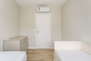 A small, clean room with a white door, a white bed, a white dresser, and a white radiator. - Near Beira-Mar | Pool | Gym #CA106 (Florianópolis)