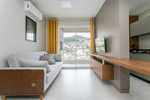 A modern apartment with a sofa, a TV, a kitchen area, and a balcony with a city view. - Near Beira-Mar | Pool | Gym #CA106 (Florianópolis)