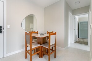 A dining area with a round table, four wooden chairs, a large mirror on the wall, and a door leading to another room. - Near Beira-Mar | Pool | Gym #CA106 (Florianópolis)