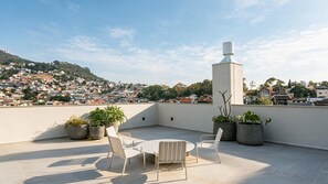 Une terrasse sur le toit, avec une table ronde et des chaises, des plantes en pot et une cheminée.
