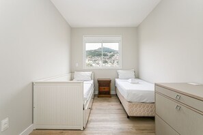 Une chambre avec deux lits, une fenêtre donnant sur un paysage vallonné, une commode en bois et un radiateur.