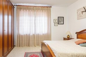 A bedroom with a bed, a nightstand, a lamp, a wardrobe, and a window with curtains. - Casa Emy da Teresina – Relax in a Green Setting Just a Stone's Throw from Alba (Reala)